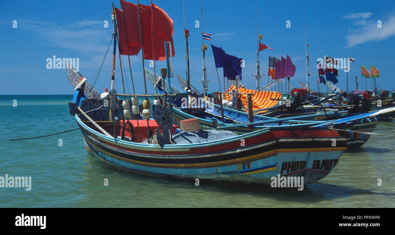 Thailand, Süden, Zeile der angedockten korlae Fischerboote mit bemalten Rümpfen, zwei Kinder schwimmen im Vordergrund. Stockfoto