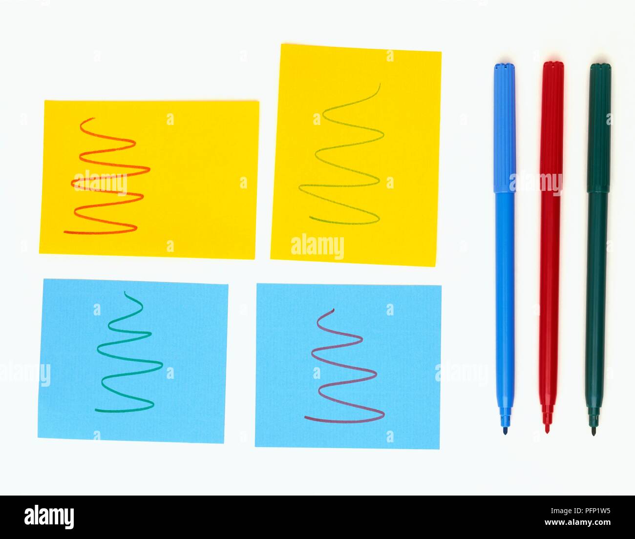 Stücke von Gelb und Blau Briefpapier mit Kringel auf ihnen gezeichnet, und drei Filzstifte Stockfoto