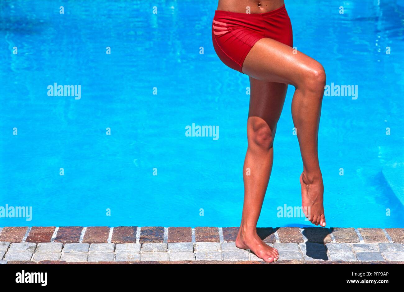 Frau im Bikini Bottoms, auf einem Bein stehen neben dem Pool, das andere Bein über das andere, close-up Stockfoto