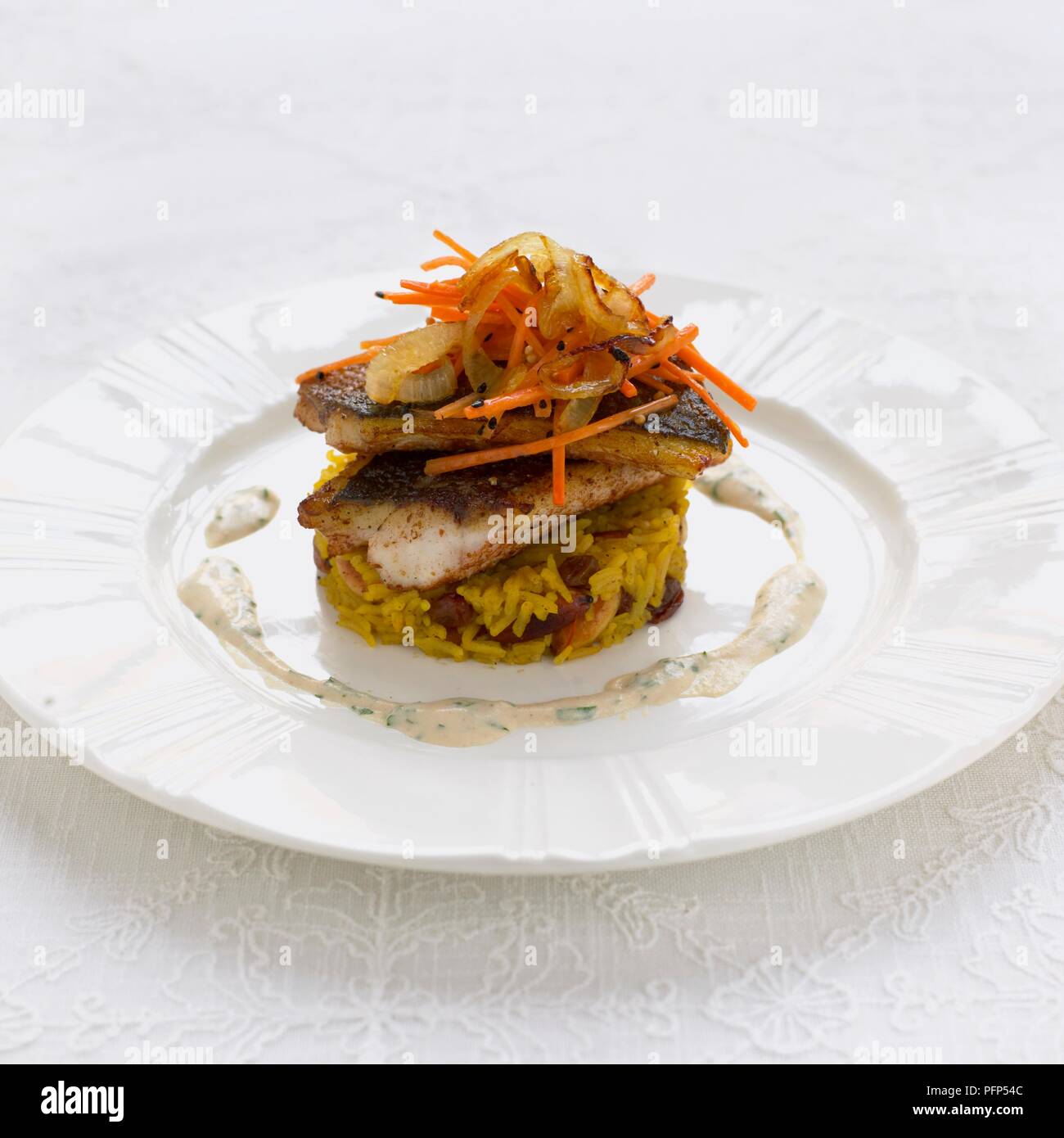 Seebarsch serviert auf Reis mit in Scheiben geschnittenen Gemüse und tahini Soße auf weiße Platte Stockfoto