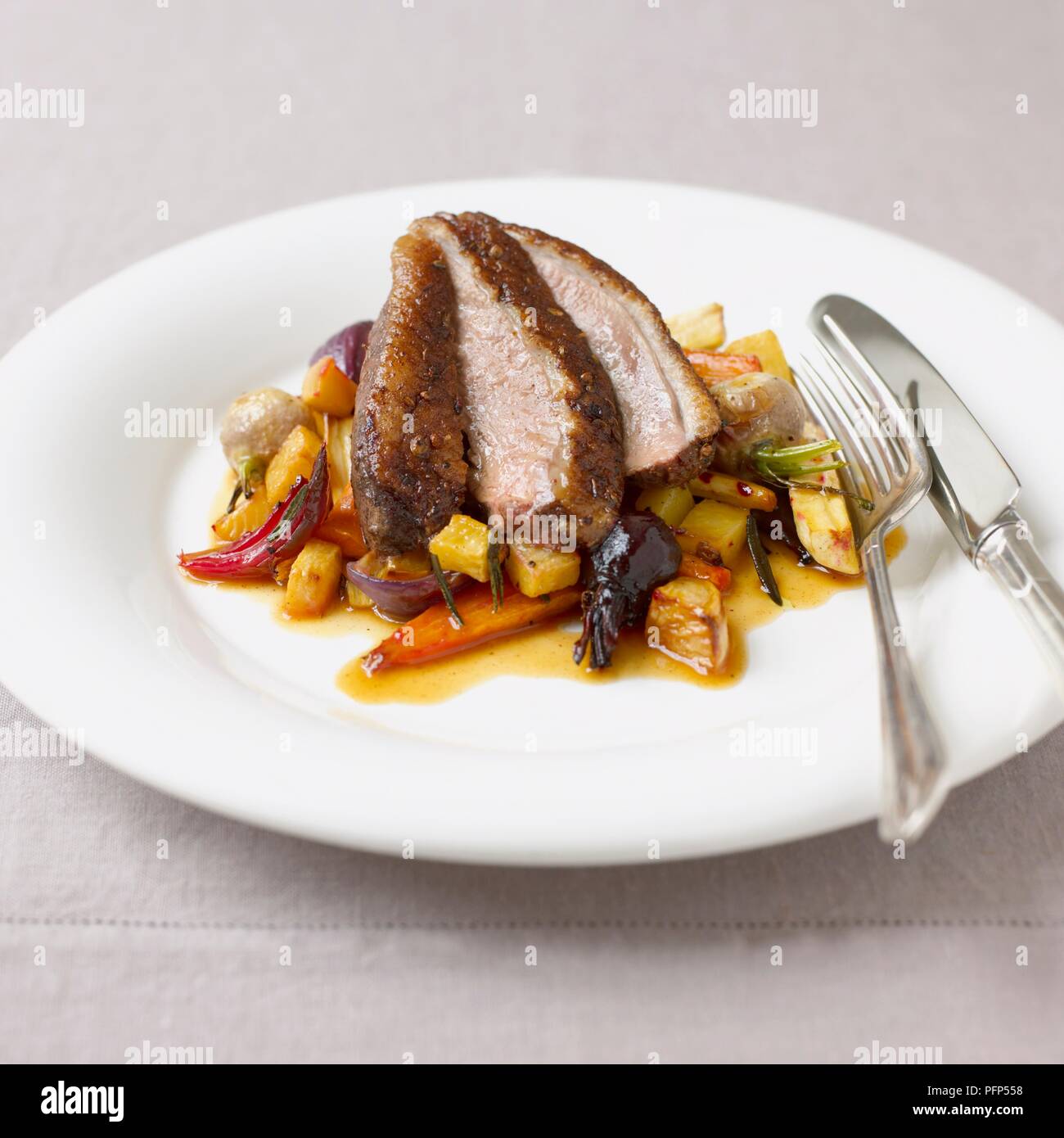 Gebratene Ente mit gehacktem und gerösteten Gemüse auf weißen Teller mit Messer und Gabel serviert. Stockfoto