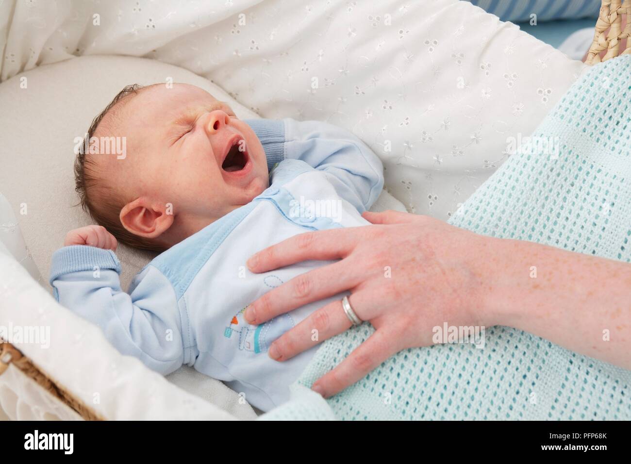 Baby boy in einem Mose Korb liegen, Gähnen, die Hand der Frau seine Brust berühren, close-up Stockfoto