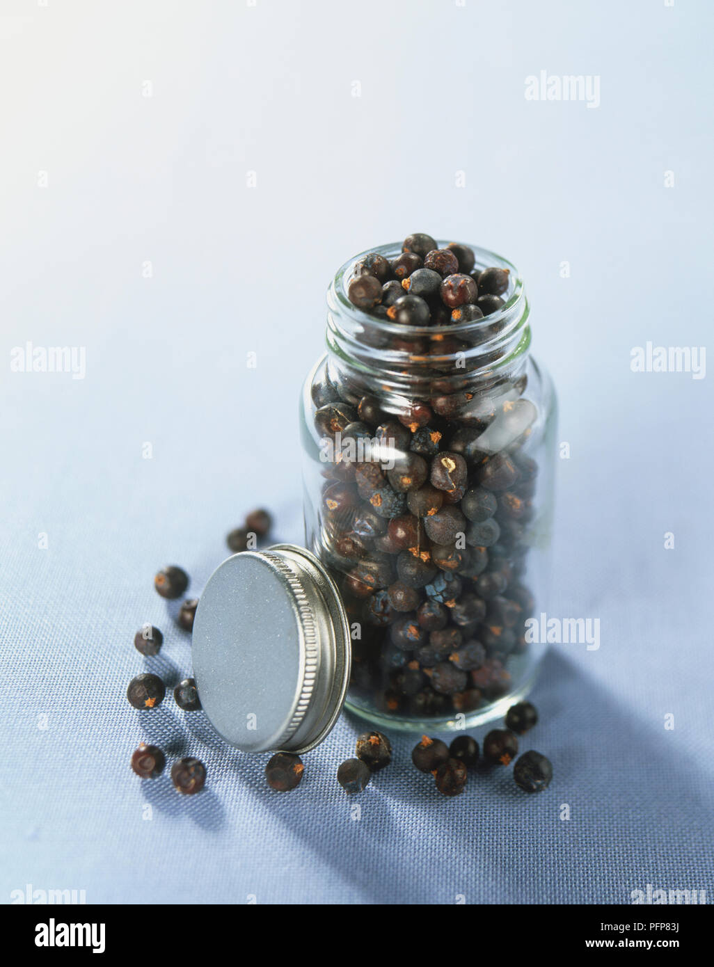 Juniperus communis, ganze getrocknete Wacholderbeeren in Glas-, Schraub- Deckel entfernt auf der Seite. Stockfoto