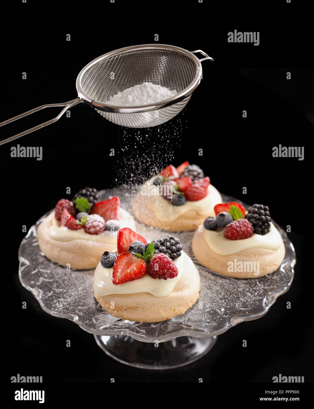 Mit Sieb zum Bestreuen Puderzucker auf Früchte meringues auf cakestand Stockfoto