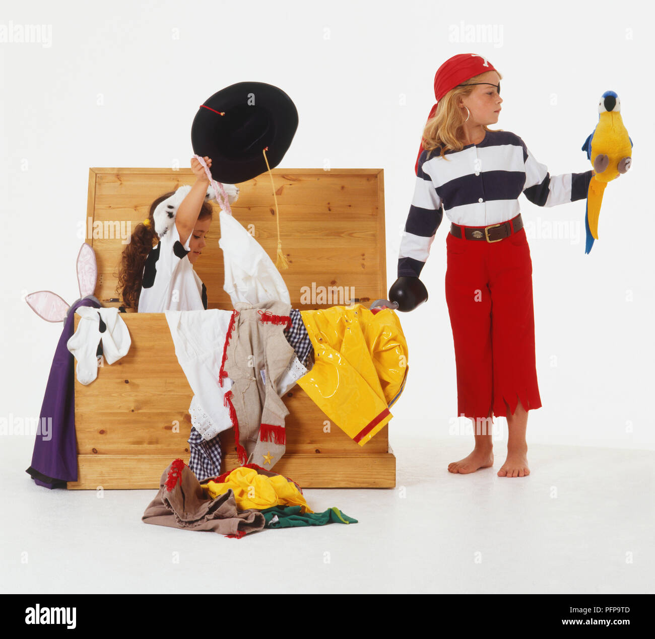 Mädchen im Pirate's Outfit, Spielzeug Papagei auf ihrem Arm, neben einem Mädchen sitzen in einem Koffer voller Kleider Stockfoto