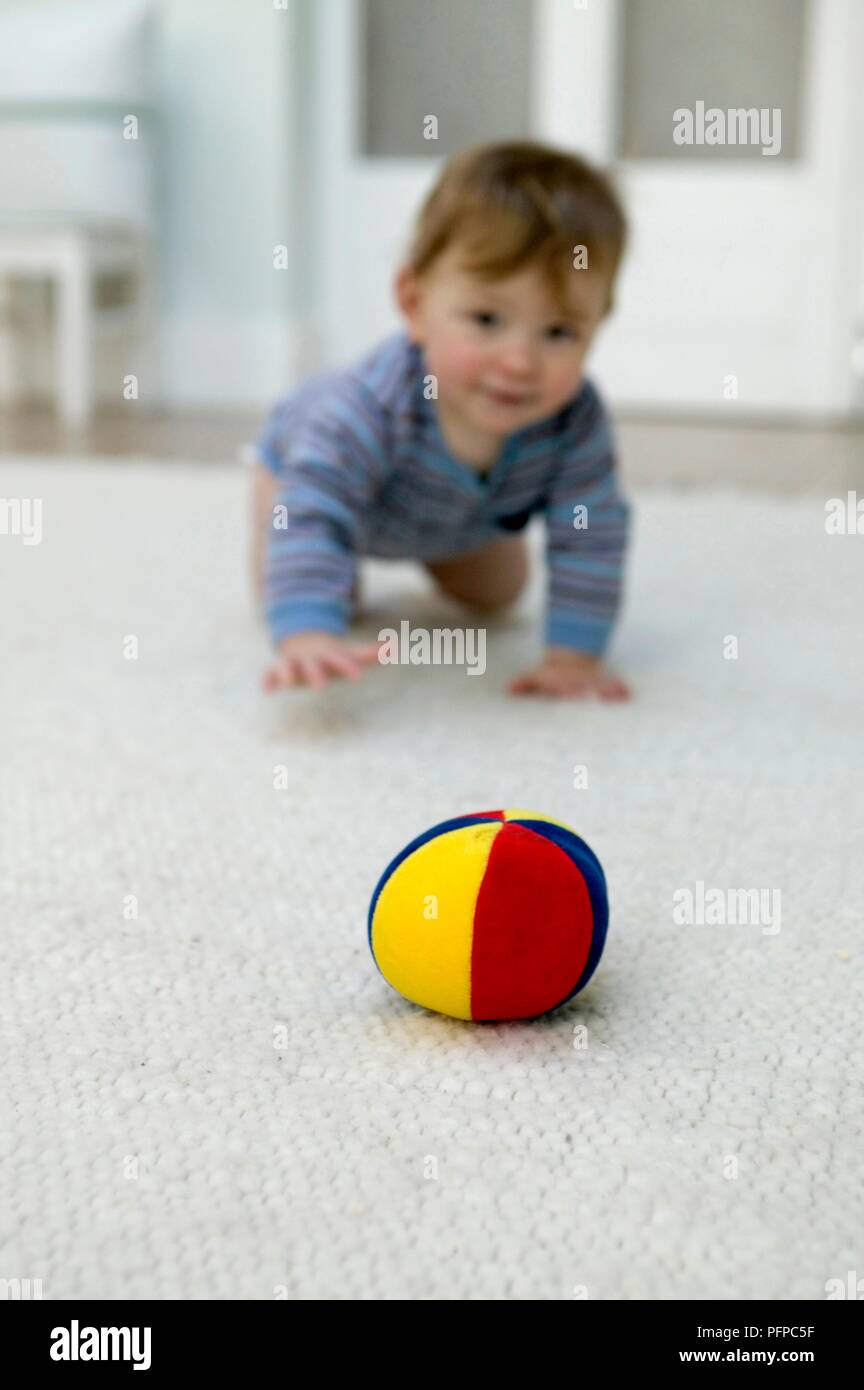Baby krabbeln in Richtung Ball auf Teppichboden, im Vordergrund Schwerpunkt Stockfoto