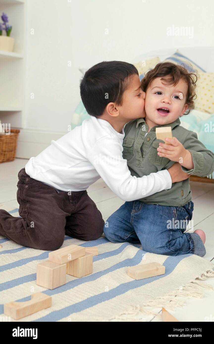 Junge küssen und umarmen Toddler, sowohl kniend auf Teppich mit Bausteine vor Ihnen Stockfoto