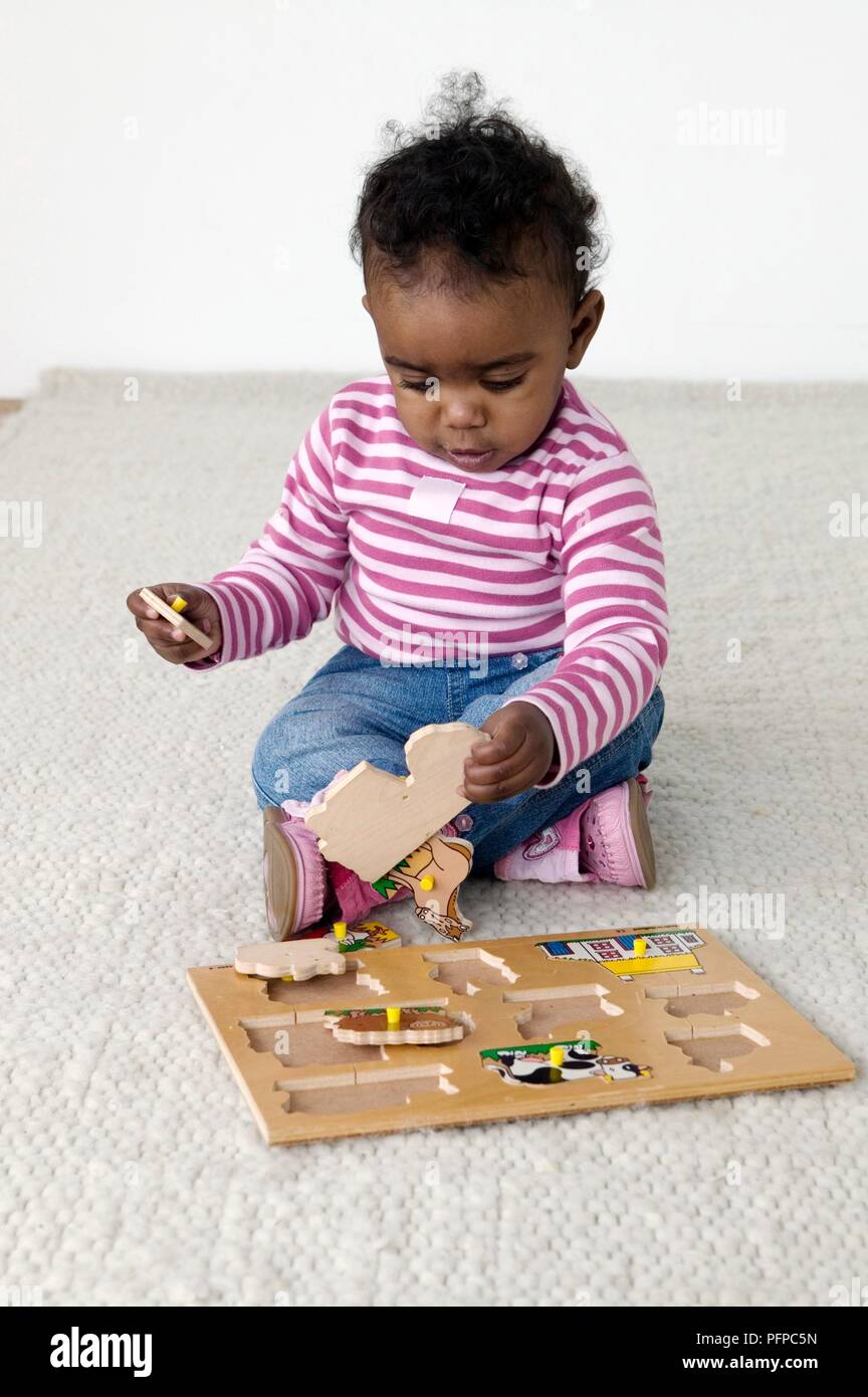 Baby Mädchen tragen Stripy top, das Spiel mit dem holzpuzzle Stockfoto