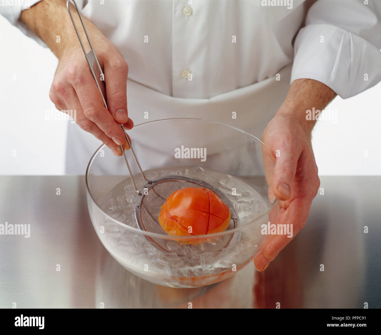 Blanchieren gekochte Tomaten in Schüssel mit Eiswasser mit Sieb Löffel Stockfoto