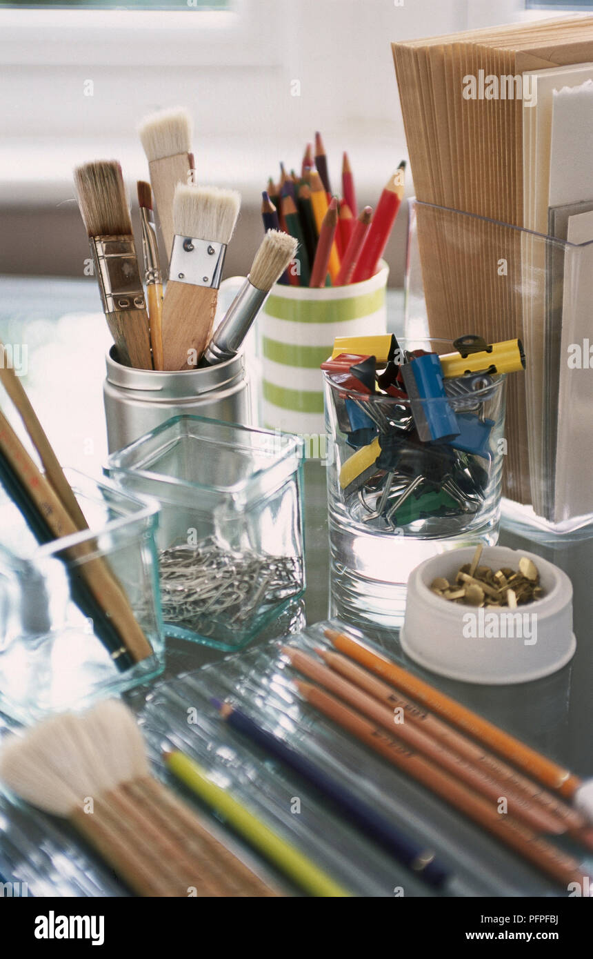Glas, tumblets, Aluminium Dosen, Tassen verwendet als improvisierten Schreibtisch - Aufräumt, Bleistifte, Büroklammern, Pinsel und Stifte, allmählich Defokussierten. Stockfoto