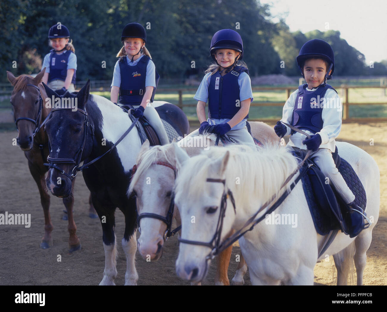 Drei junge Mädchen und junge sitzt auf Ponys in einer Reihe im Fahrerlager Stockfoto