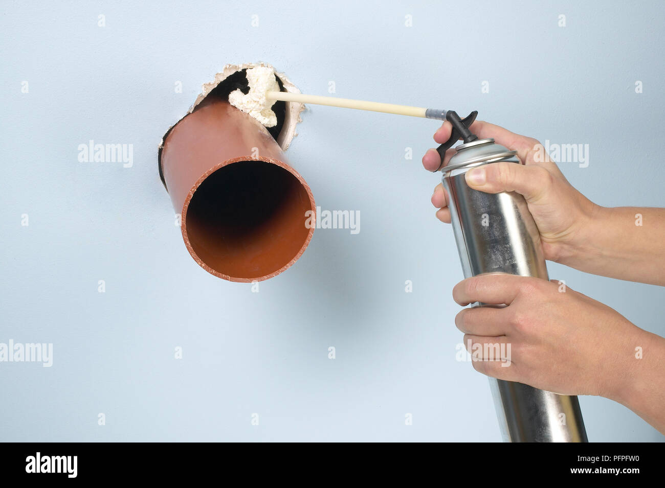 Spritzen Bauschaum in ein Loch über ein Rohr in der Wand Stockfoto