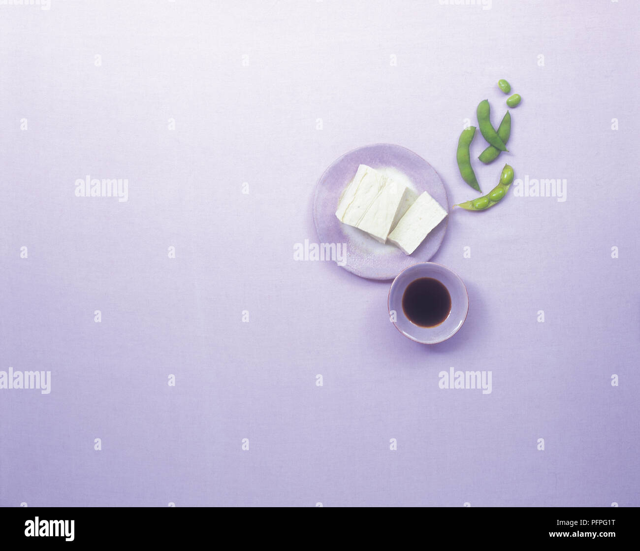 Tofu in kleine lila Platte, grüne Sojabohnen und dunkle Sojasauce in kleine lila Schale Stockfoto