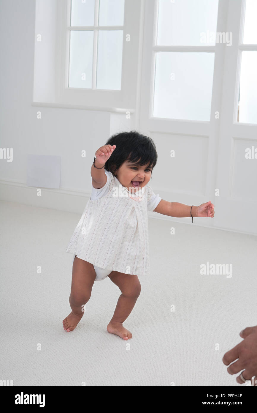 Kleinkind Mädchen entlang Teppichboden mit erhobenen Armen Stockfoto