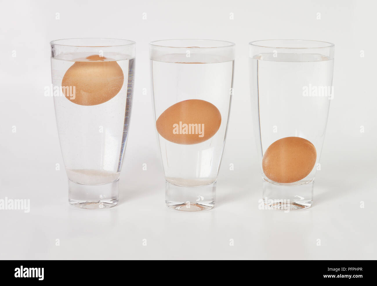 Drei Gläser Wasser, Eier, jedes Ei auf verschiedenen Ebene im Glas (Waschbecken oder float Ei frische Test) Stockfoto