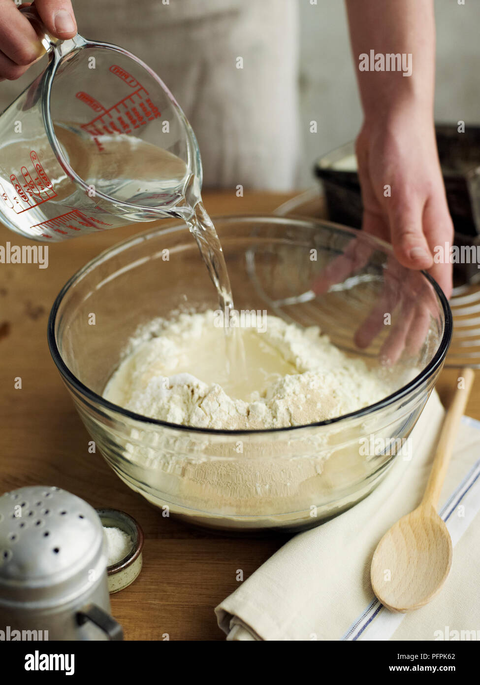 Das Gießen von Wasser aus der Kanne zu mischen mit anderen Zutaten in der Schüssel (Brot) Stockfoto