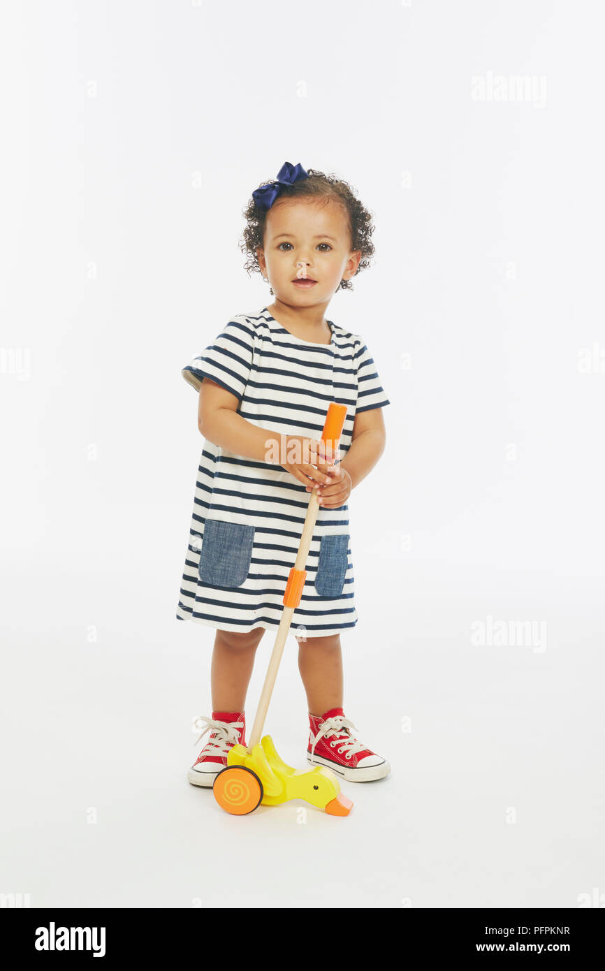 Kleines Mädchen in gestreiften Kleid spielen mit Schiebe Spielzeug (Modell Alter - 19 Monate) Stockfoto