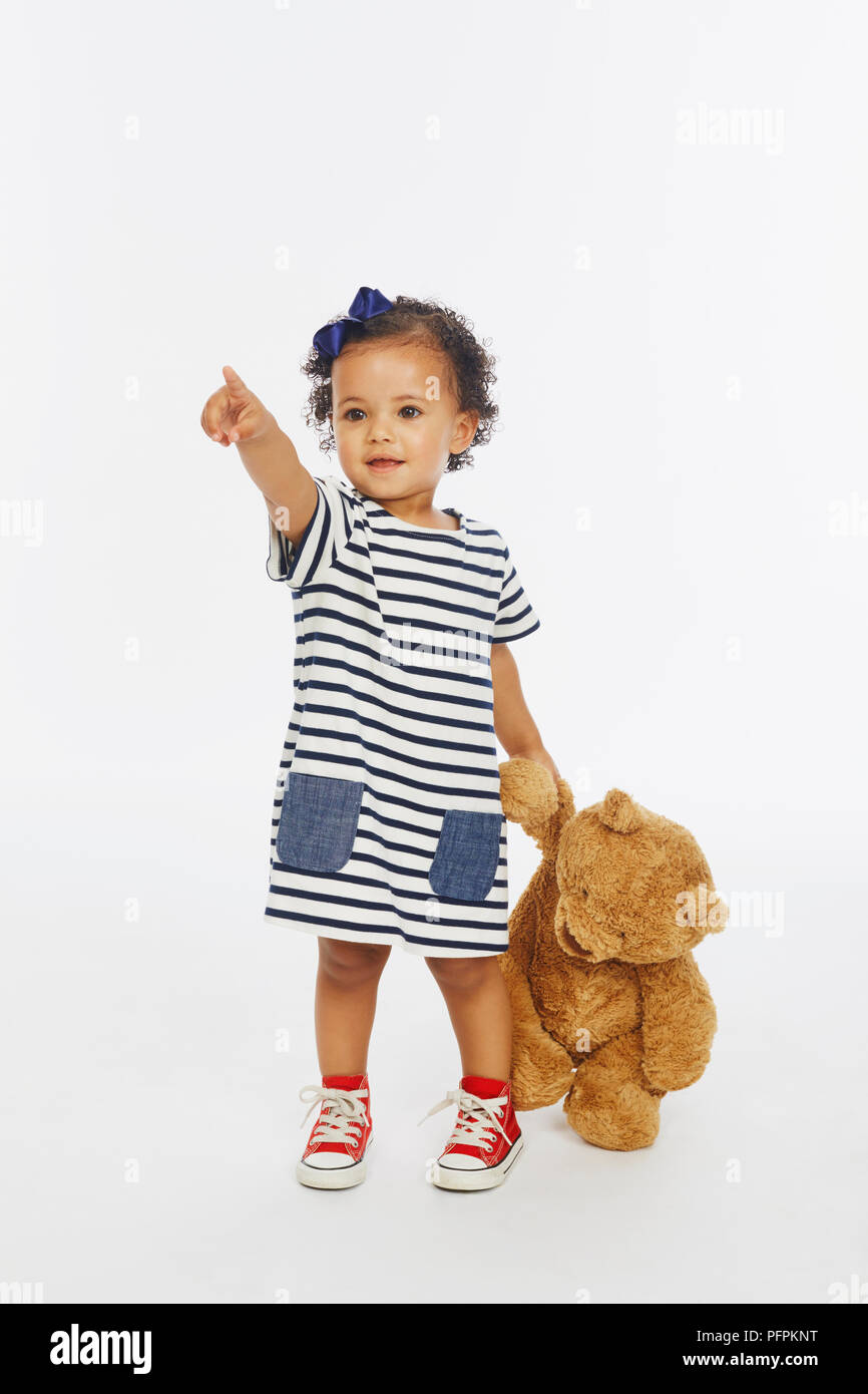 Kleines Mädchen in gestreiften Kleid spielen mit Bär (Modell Alter - 19 Monate) Stockfoto