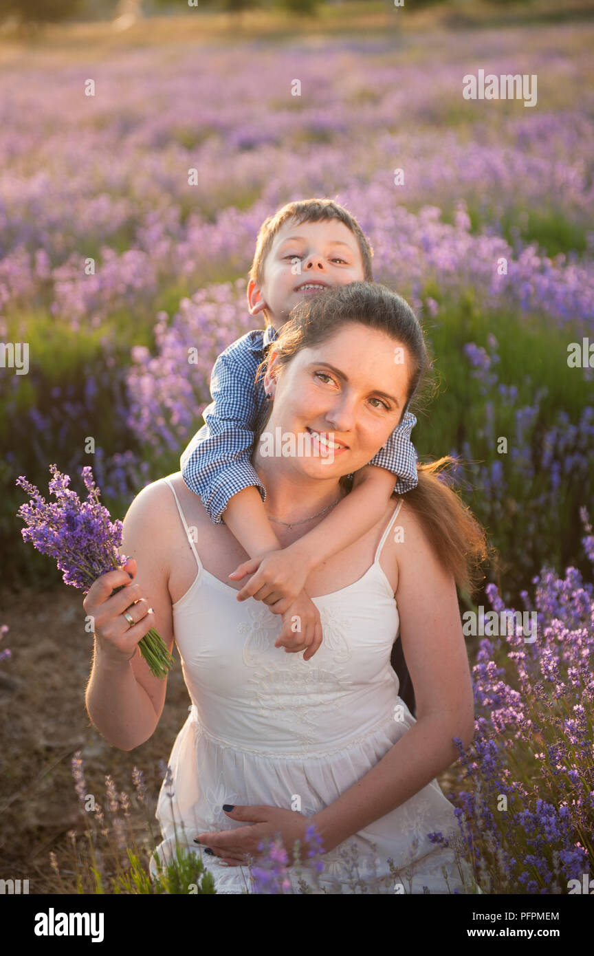 Kleines Kind umarmen hid-Mutter mit Blumenstrauß von wilden Blumen in blühenden Feld Stockfoto