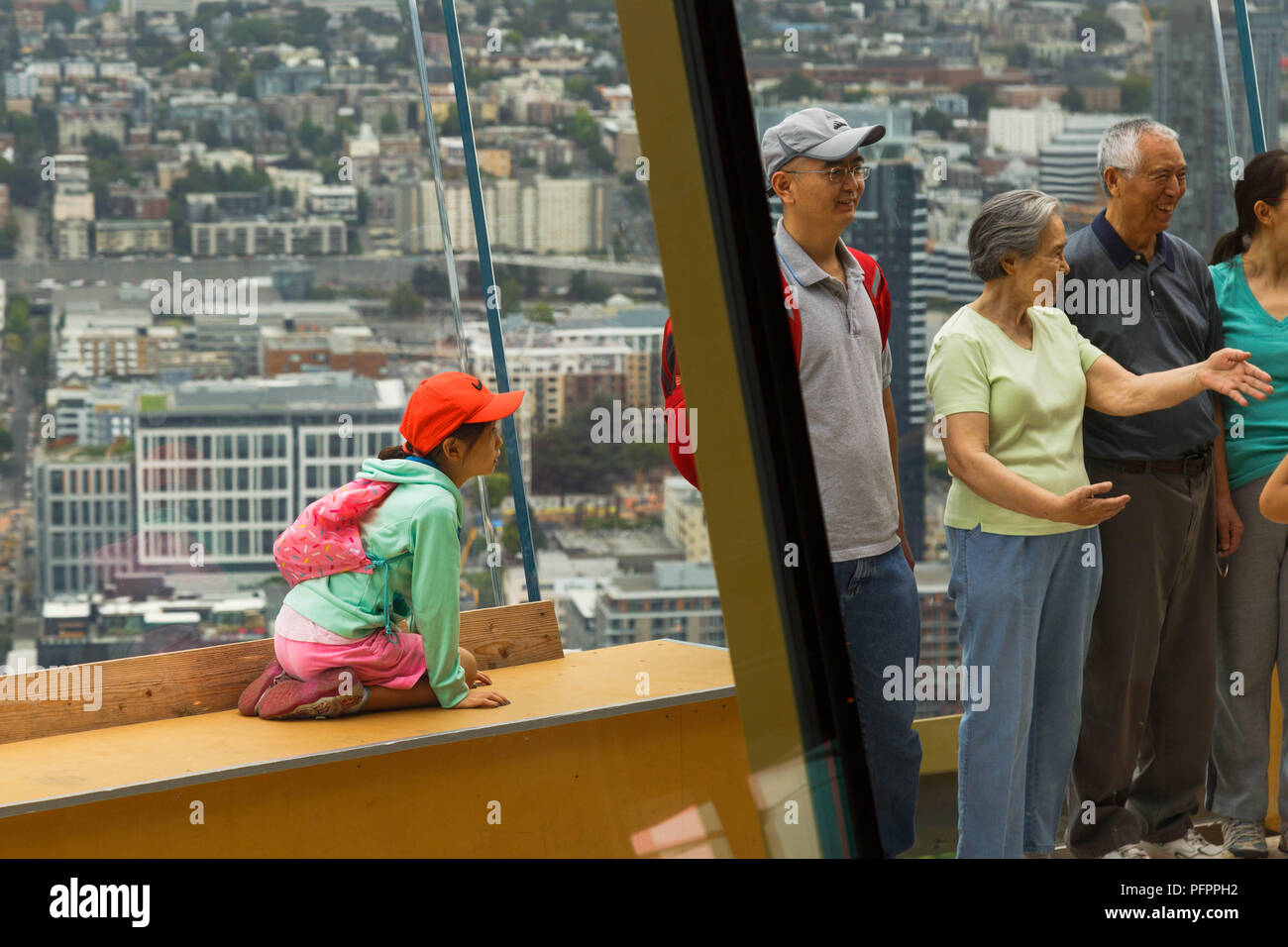 Ein Mädchen schaut neugierig an ihre Familie sprechen und lachen neben ihr an der Spitze der Space Needle Observation Deck, Seattle, Washington, USA. Stockfoto