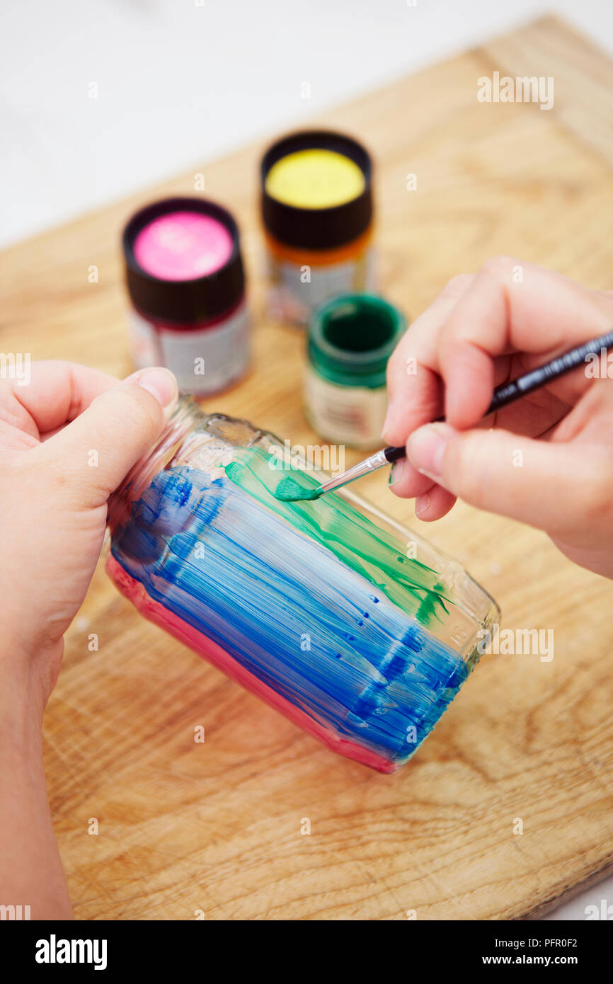 Mädchen Malerei Glas Glas mit grün, blau und rosa Streifen, mit Pinsel im Hintergrund auf hölzernen Tisch Stockfoto