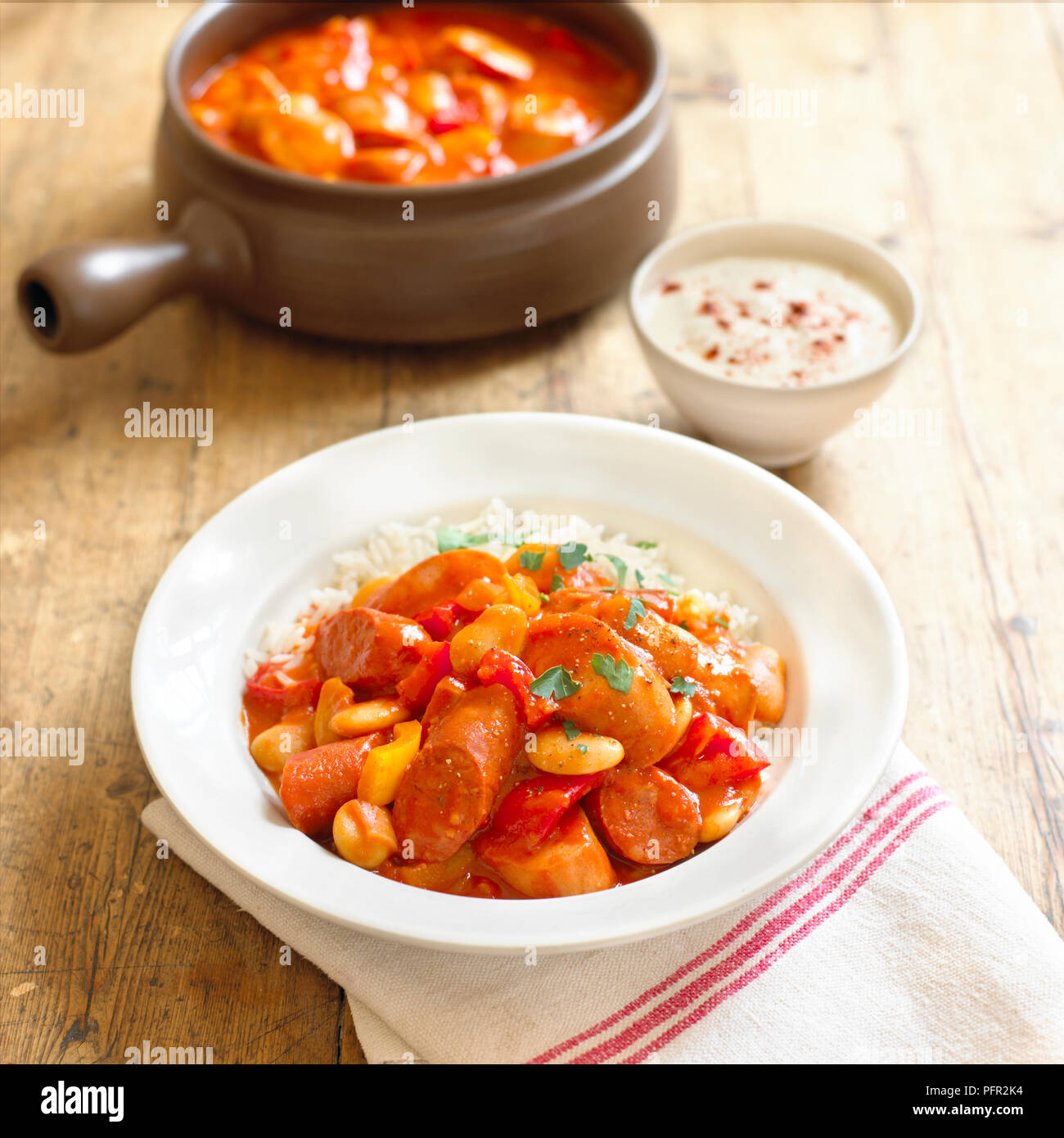 Wurstgulasch serviert mit weißer Reis in Weiß Schüssel und Klein Schüssel saure Sahne, close-up Stockfoto