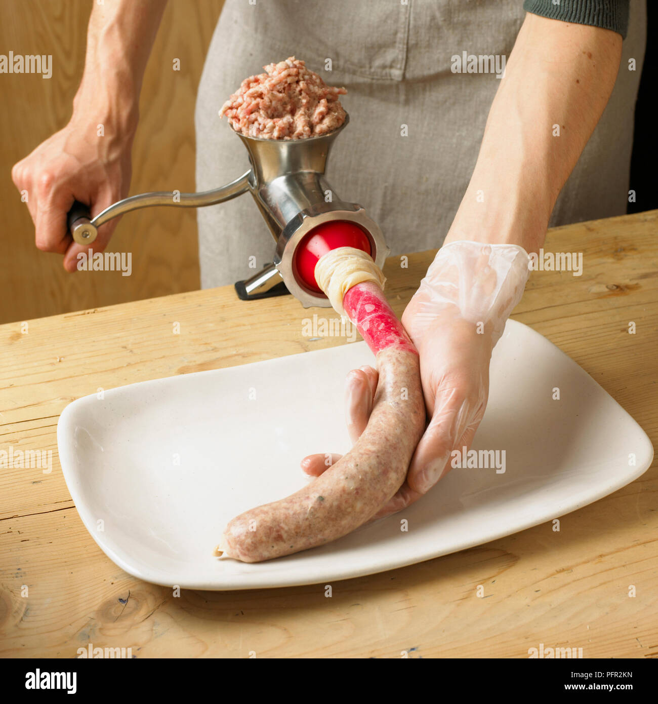 Mann mit fleischwolf Wurst Gehäuse mit Hackfleisch Schwein am Küchentisch zu füllen, close-up Stockfoto