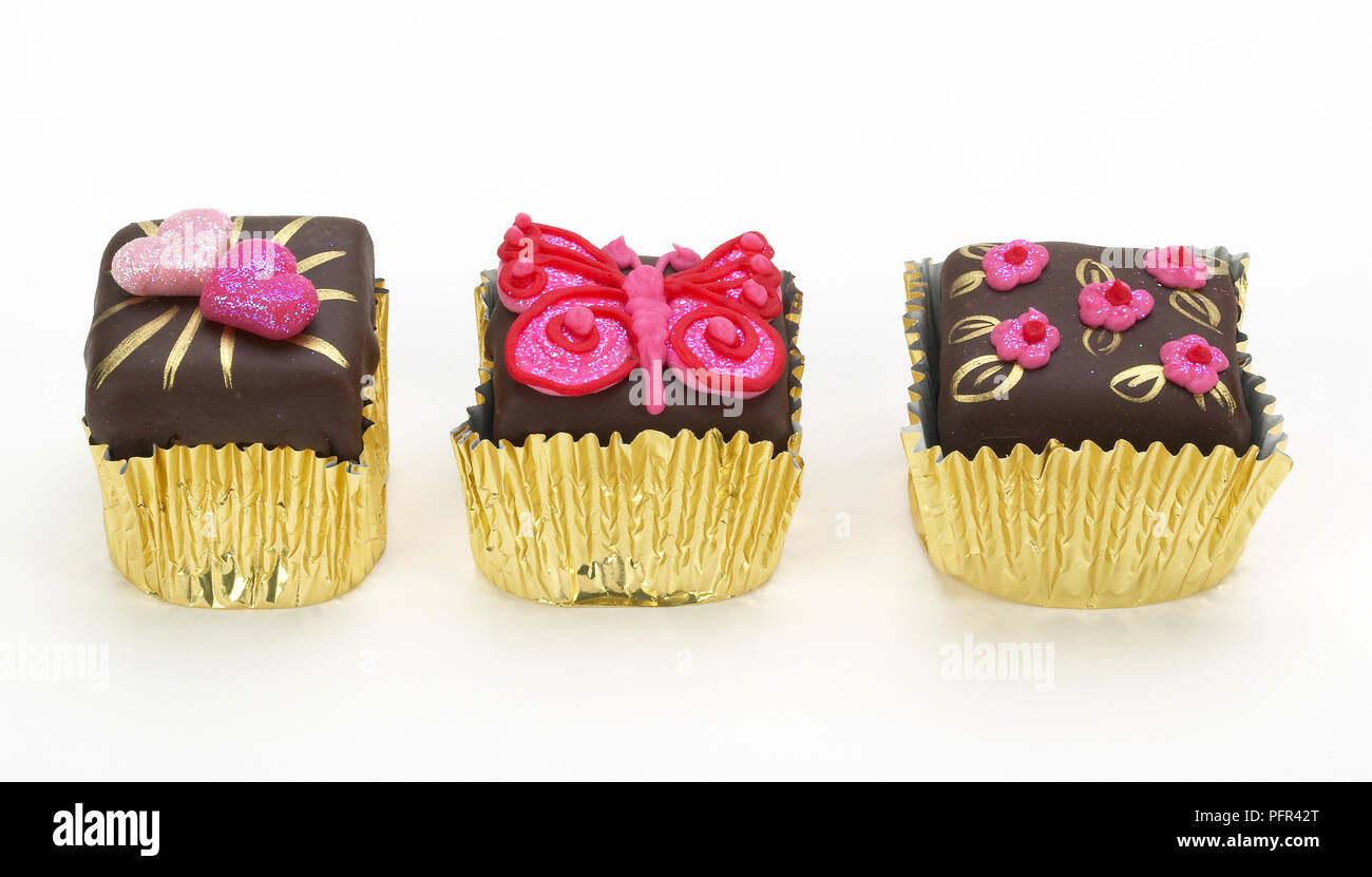 Kleine Schokolade Kuchen mit rosa Zuckerguss, in gold Kuchen Fällen Stockfoto