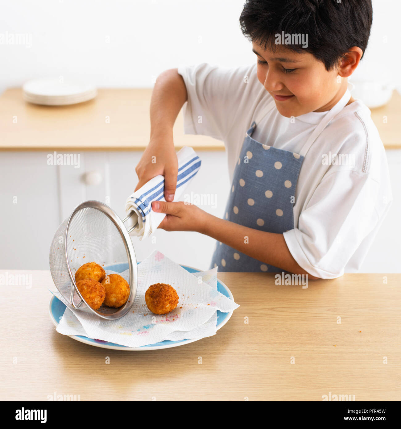 Junge gießen Sieb mit vier frittierte Reisbällchen auf Platte, 9 Jahre Stockfoto