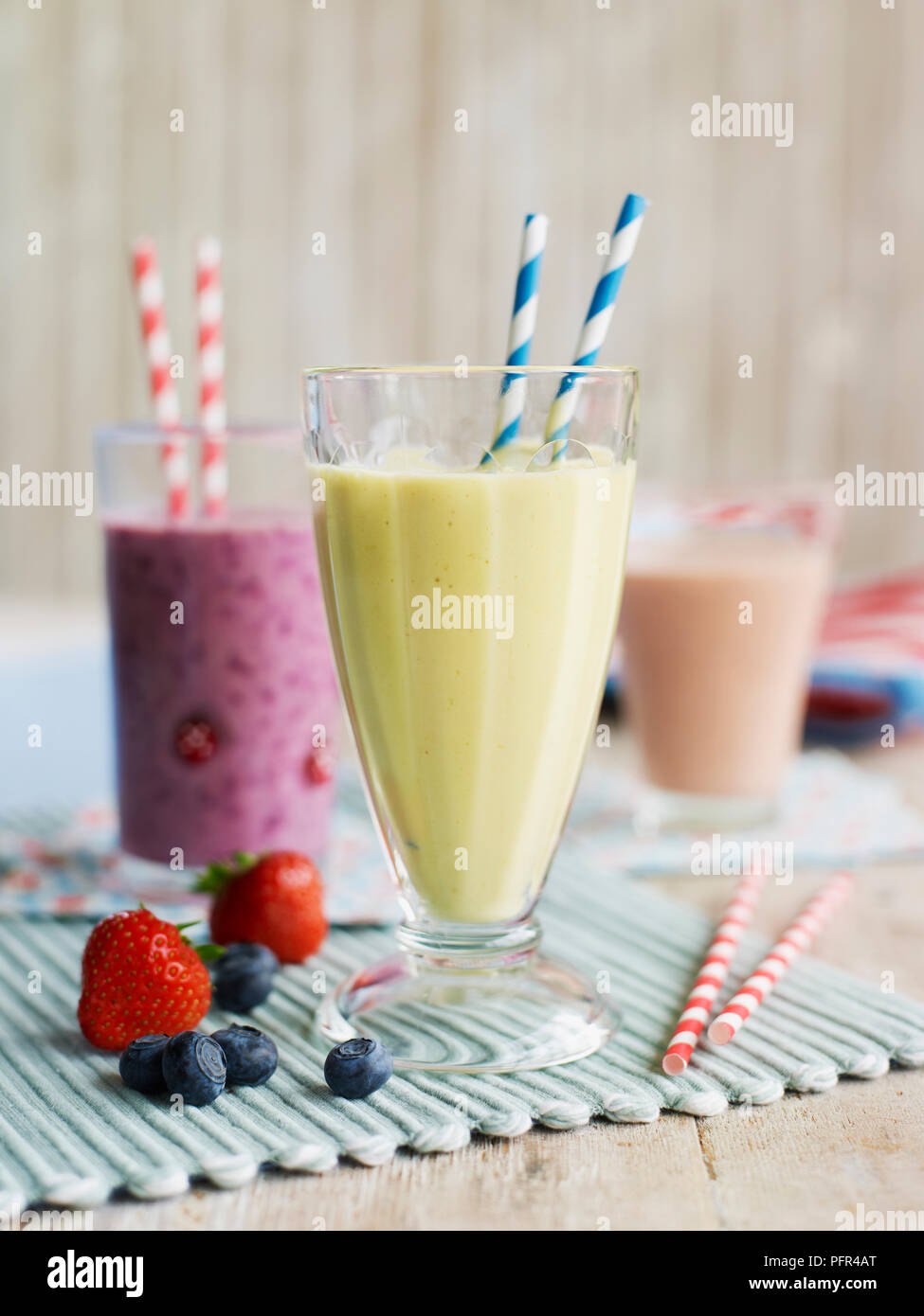 Gläser mit Trinkhalme mit verschiedenen Frucht-smoothies, Banane und Mango im Vordergrund, und Erdbeere und Heidelbeere weiter zurück Stockfoto