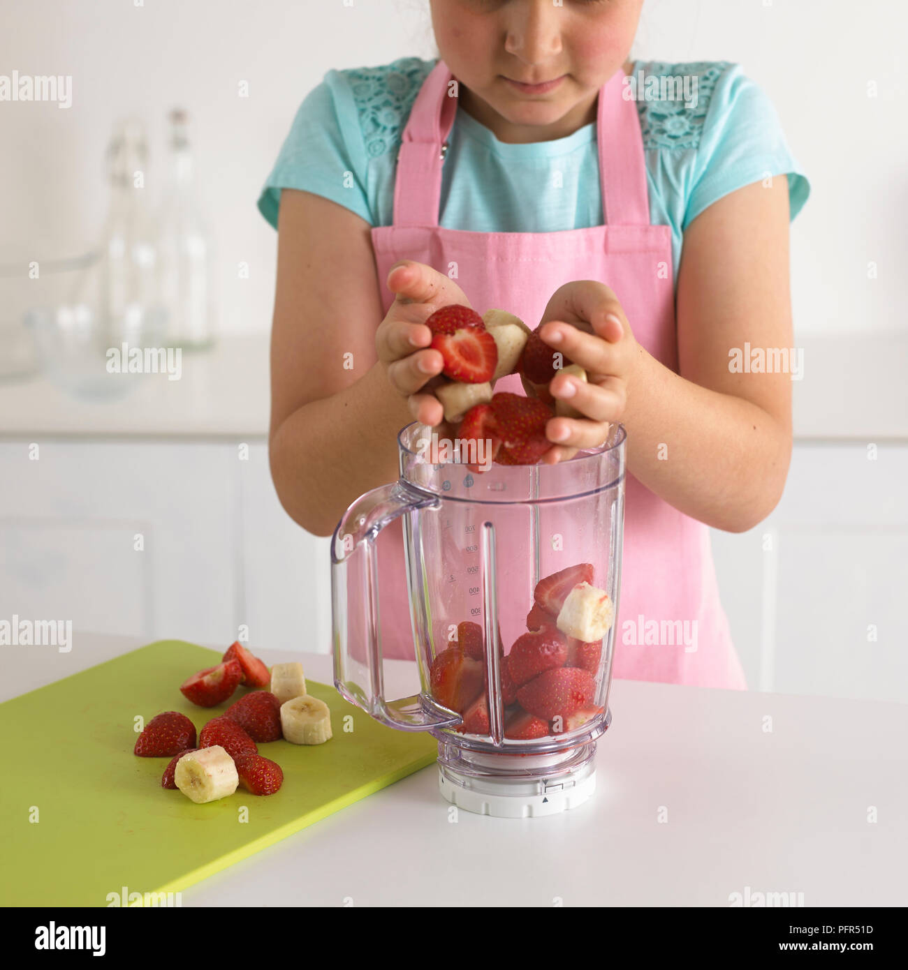 Mädchen legen Erdbeeren und Bananen in einen Mixer, 8 Jahre Stockfoto