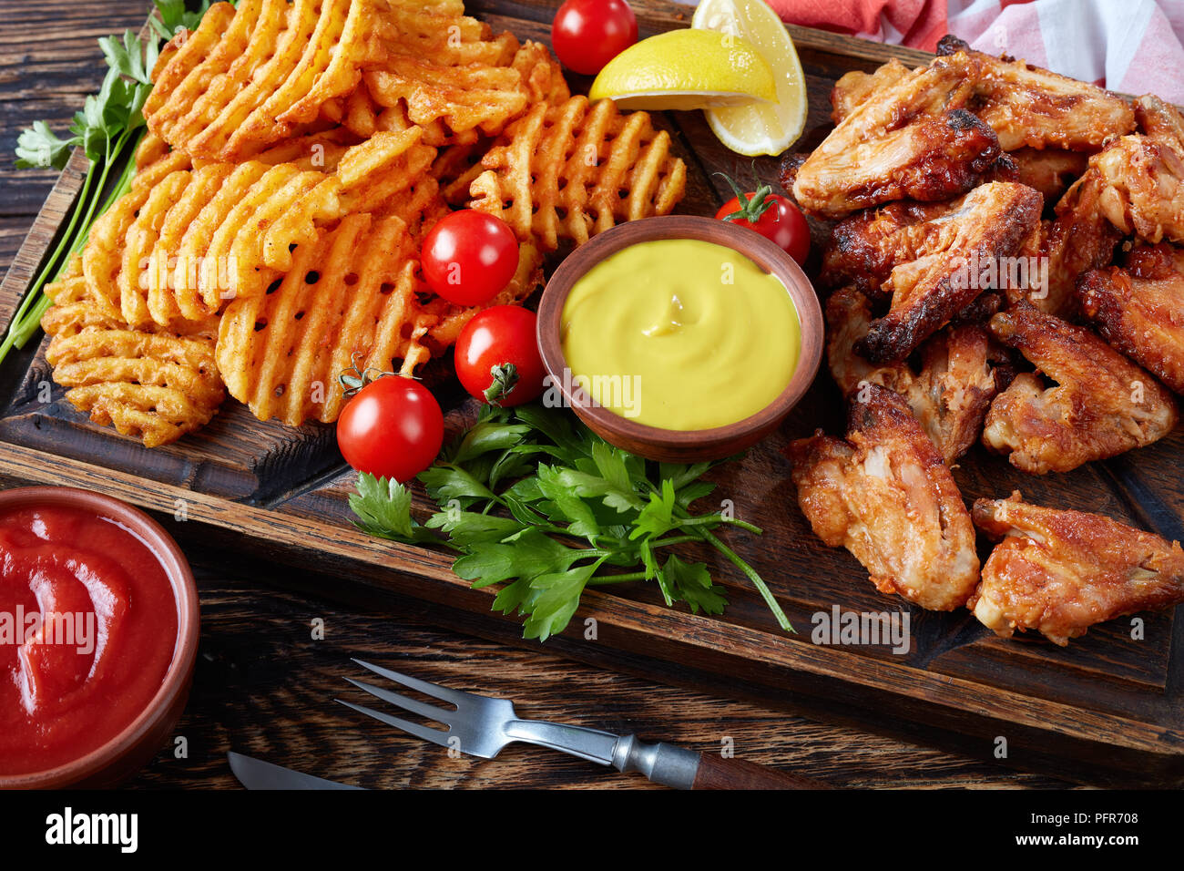 Nahaufnahme der Fried Chicken Wings, knusprige Pommes frites Potato Kreuz und Quer auf einem Ton Platten auf einem Holztisch mit Senf und Tomatensauce eintauchen, Ansicht von eine Stockfoto