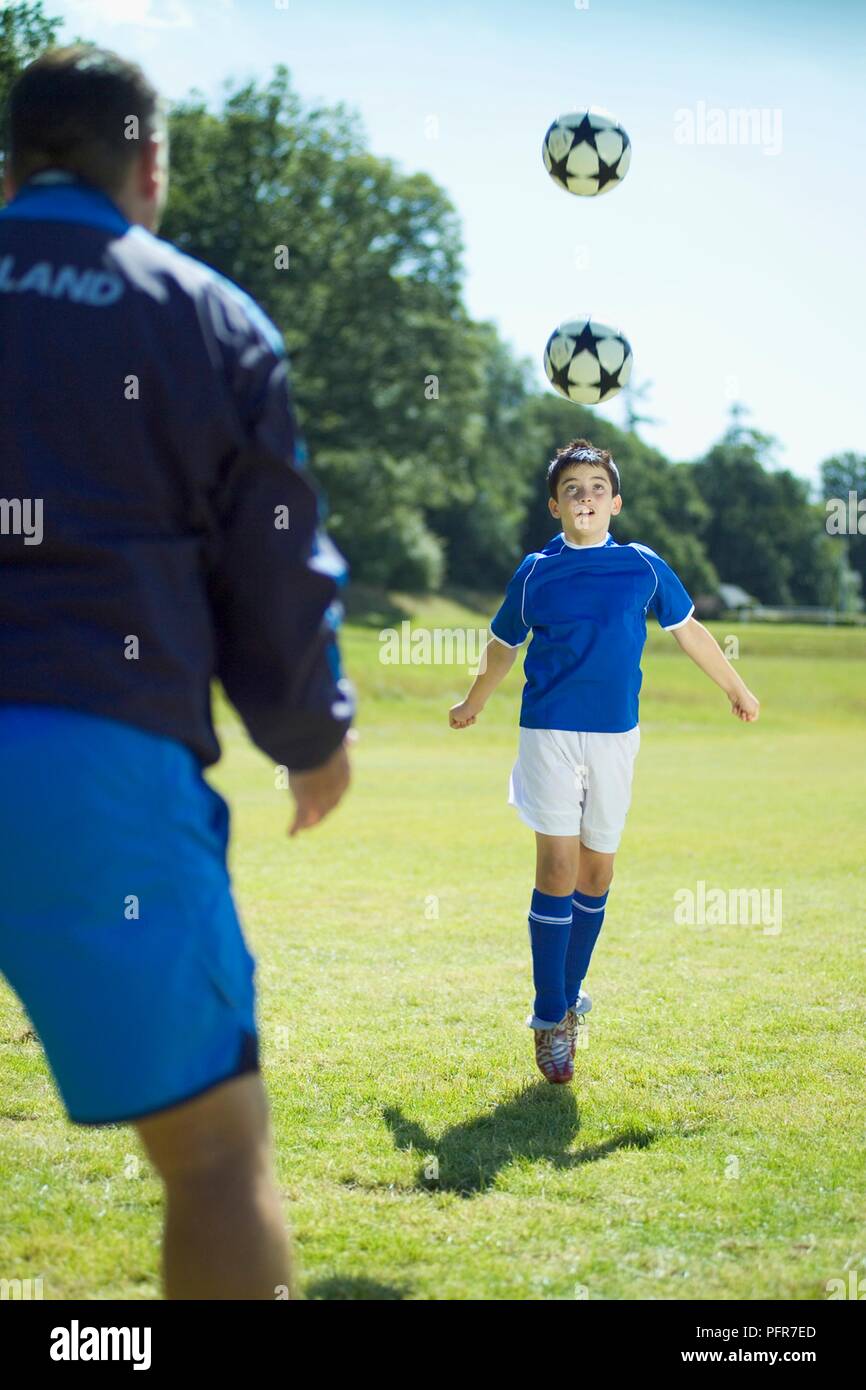 Junge Fußball-Spieler üben defensive Kopfzeilen, Trainer stehen in der Nähe Stockfoto