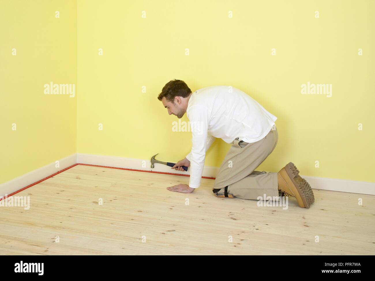 Man hämmern Teppich Greifer Stangen an der Kante der Zimmer mit gelben Wänden Stockfoto
