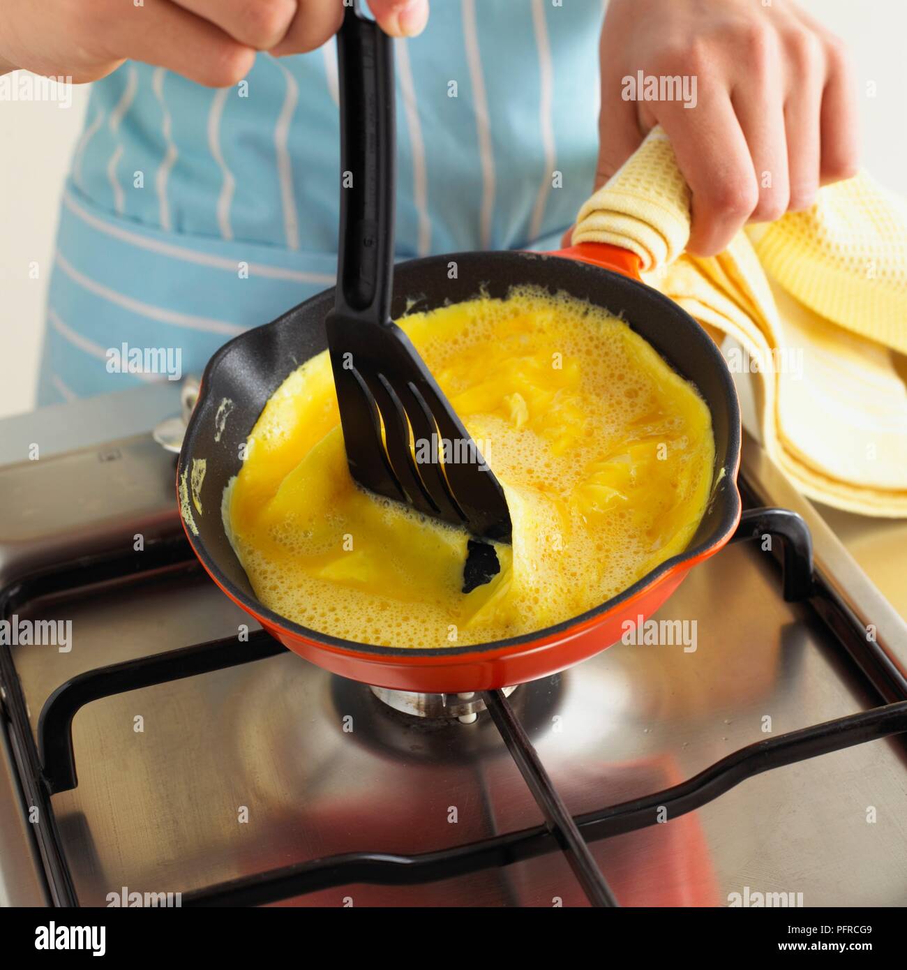 Junge Holding heiße Griff der Pfanne mit Geschirrtuch und mit Spachtel omeltte Mischung zu bewegen Stockfoto