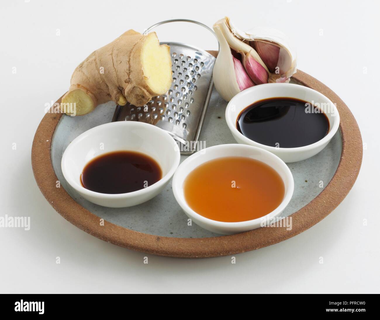 Knoblauch, Ingwer, eine Reibe, und Schüsseln mit Balsamico, Honig und Sojasauce auf einer Platte angeordnet Stockfoto
