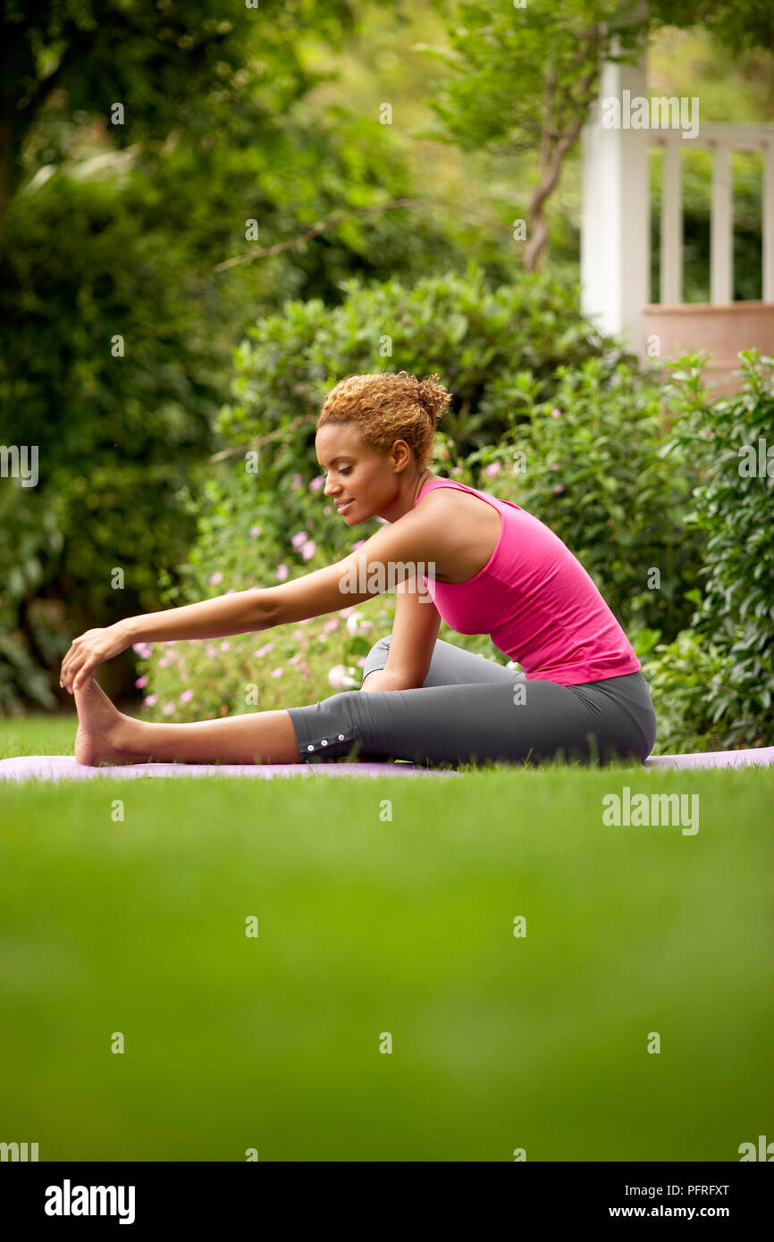 Junge Frau in Leggings und rosa Top im Garten sitzen, Stretching Übung Stockfoto