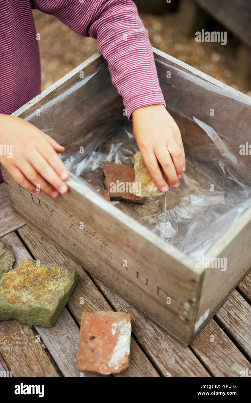 Mädchen legen Steine im Holzkasten gesäumt mit Kunststoff Stockfoto