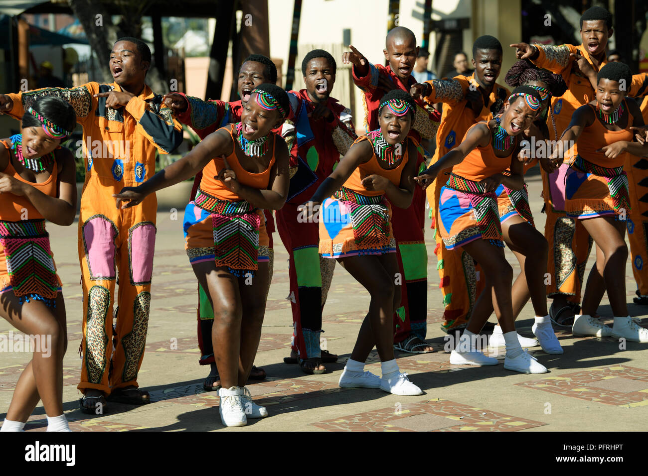 Junge erwachsene Männer und Frauen in die Zulu Kultur Kostüm tanzen und singen die Besucher uShaka Marine World, Durban, KwaZulu-Natal zu unterhalten Stockfoto