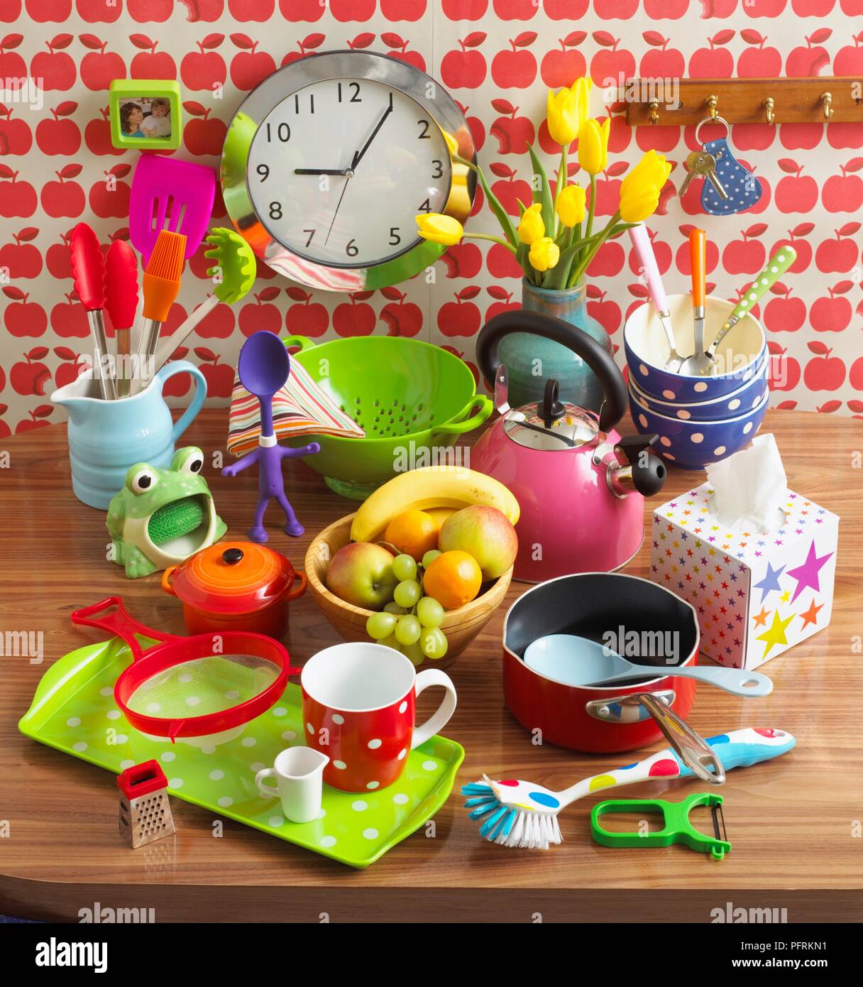 Spielzeug, Geschirr, Wasserkocher, Schüssel mit Obst, Blumen und die Uhr an der Wand in der Küche Stockfoto