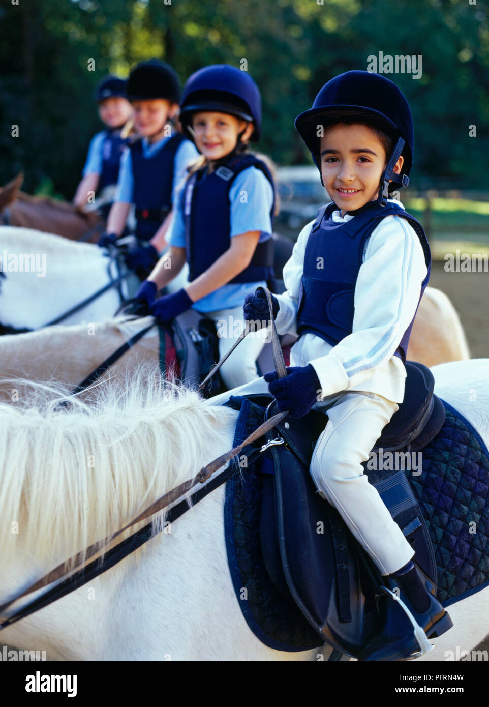 Vier Kinder auf Ponys, Seite an Seite, an der Kamera auf der Suche Stockfoto