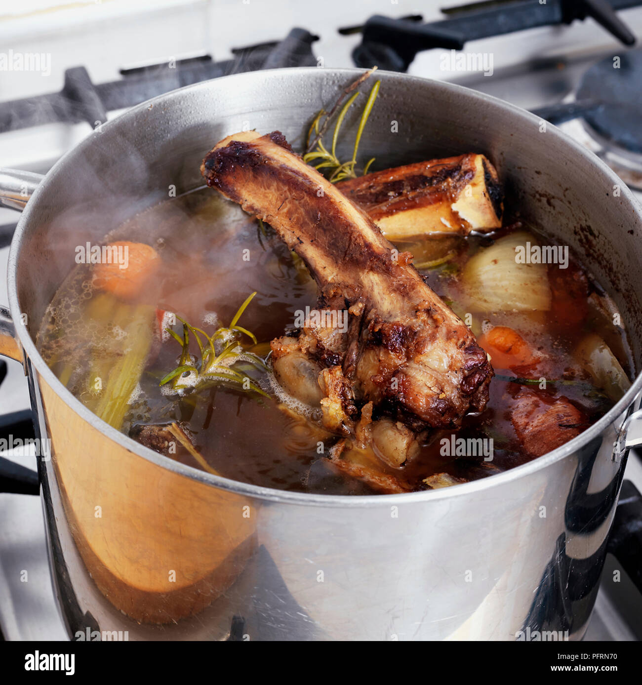 Die Lager in den großen Pan, sanft simmering Rindfleisch Knochen mit Karotte, Sellerie, Zwiebel und Rosmarin auf Gasherd Stockfoto