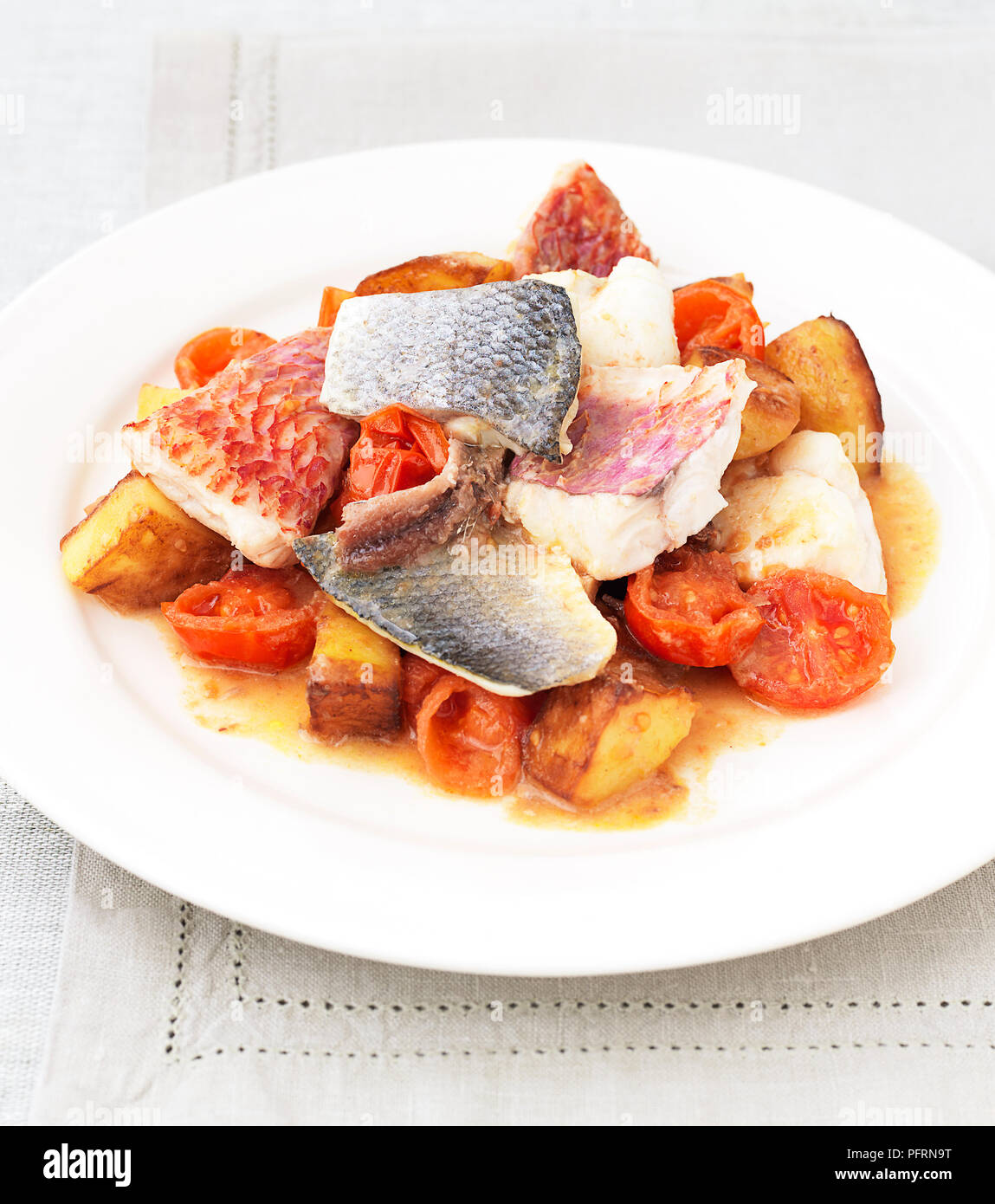 Brocken der Fisch mit Tomaten, Kartoffeln und Zwiebeln auf weiße Platte serviert auf Tischdecke, close-up Stockfoto