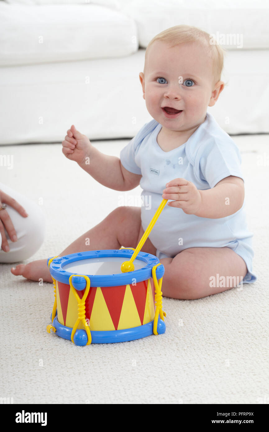 Baby Boy (10 Monate) sitzt auf dem Boden spielen mit einem Spielzeug drum Stockfoto