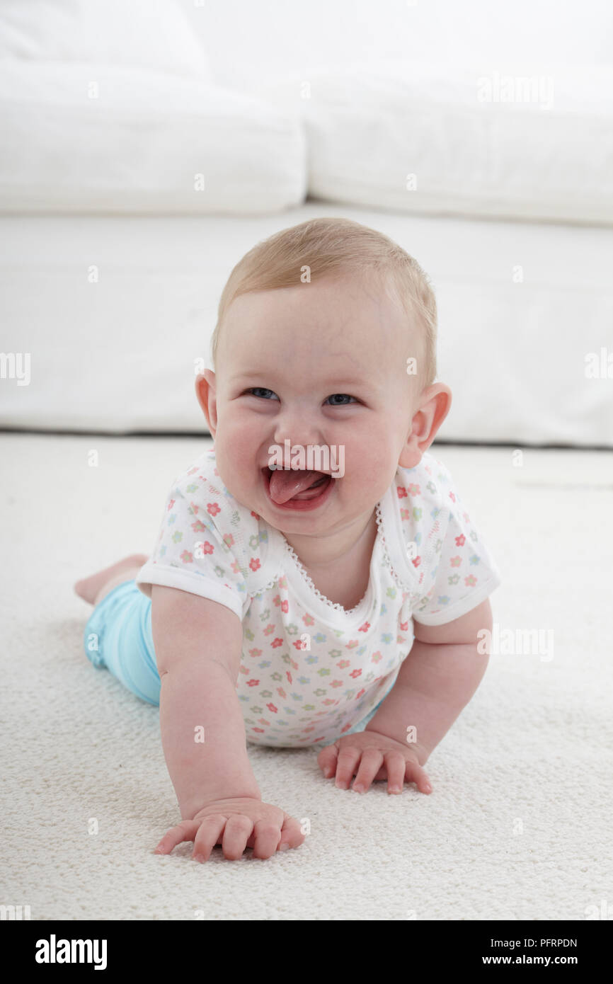 Baby (9 Monate) Kriechen auf dem Boden, ihre Zunge heraus Stockfoto