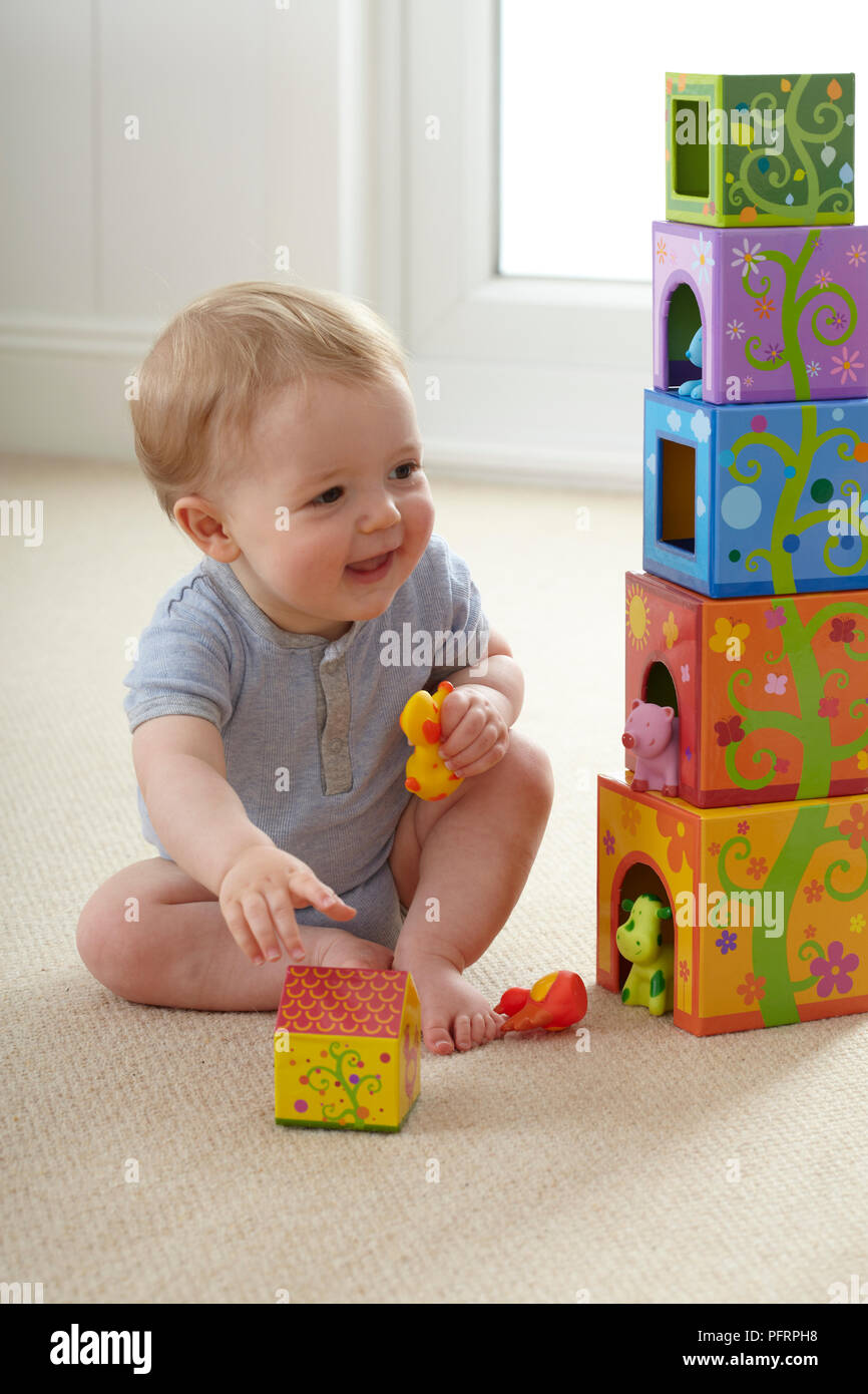 Baby Boy (12 Monate) sitzt auf dem Boden neben der Kisten zu stapeln, mit Spielzeug Tiere Stockfoto