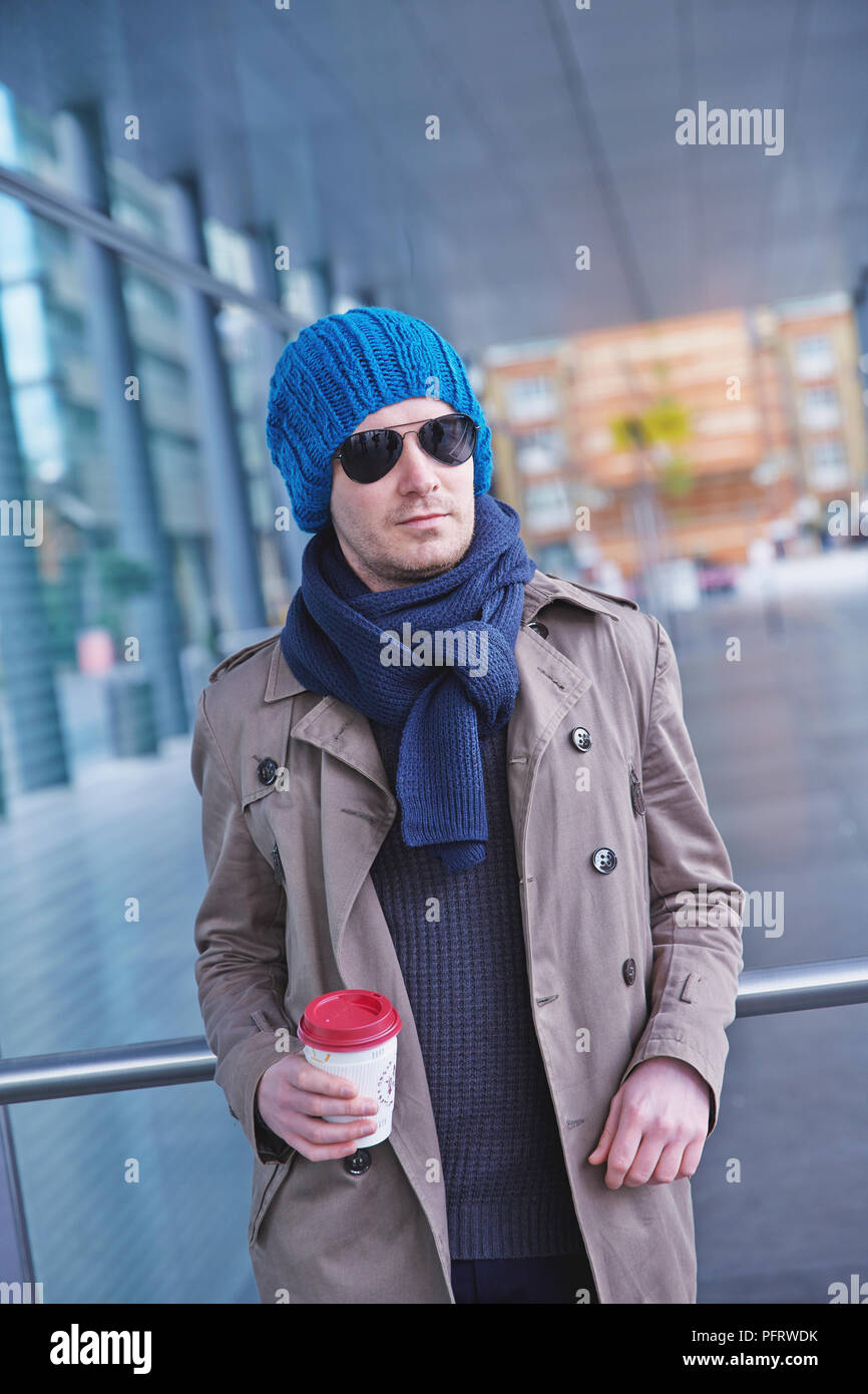 Mann gegen eine Bar mit einem heißen Getränk, ein blaues, lockeres Beanie lehnend. Stockfoto