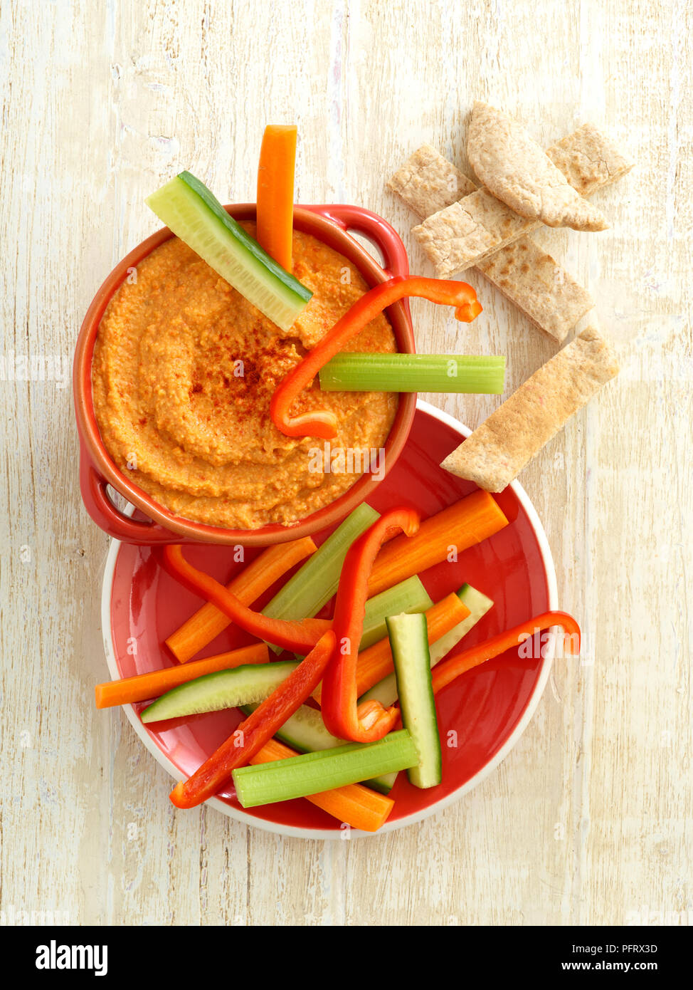 Overhead shot aus einer Schüssel rote Paprika Stil Houmous, serviert mit Pitta Brot und Schlagstöcken der Gurke, Paprika und Möhre Stockfoto