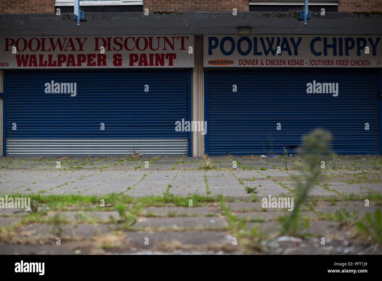 Unkraut vor geschlossene Geschäfte in das verlassene Poolway Einkaufszentrum in Garretts Green, Birmingham. 1961 errichtet, es war einst ein blühendes Handelszentrum mit lokalen und grossen Marke Geschäfte, hat aber eine Geisterstadt geworden, nur einige Monate nach dem Schließen. Stockfoto