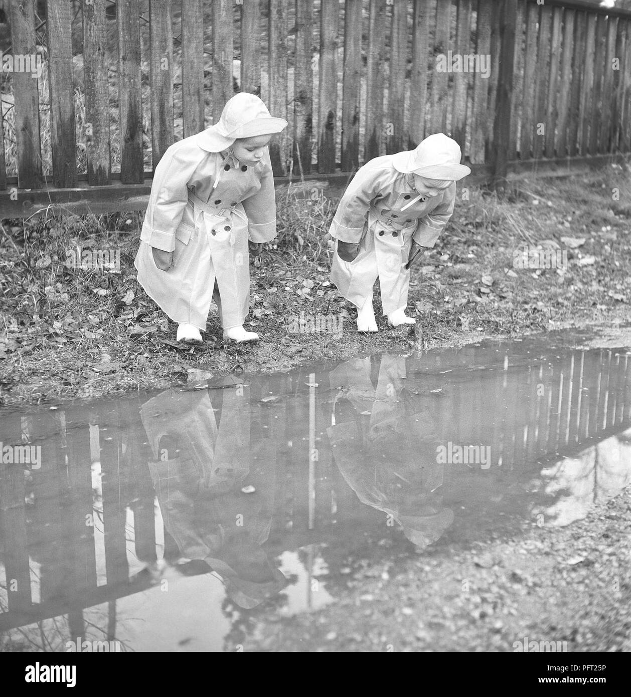 1950er Jahre Kinder in Regenkleidung. Zwei Kinder stehen an einer Wasserpfütze in Regenmänteln und Gummistiefeln. Schweden 1952 Ref. BH91-9 Stockfoto